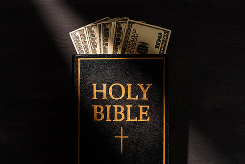top view of holy bible with money on dark background with sunlight