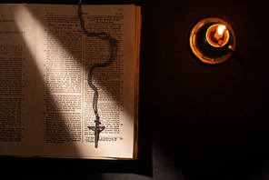top view of holy bible with cross and candle on dark background with sunlight