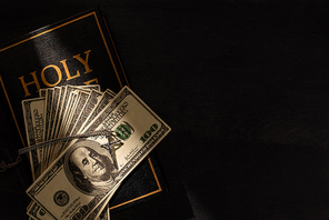 top view of holy bible with money and cross on dark background with sunlight