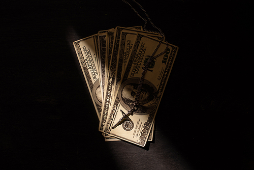 top view of money and cross on dark background with sunlight