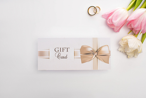 Top view of flowers, wedding rings and gift card on white background