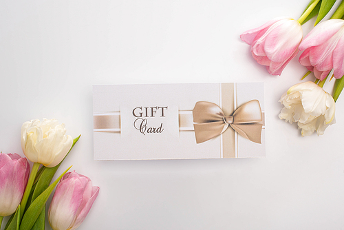 Top view of gift card near tulips on white background