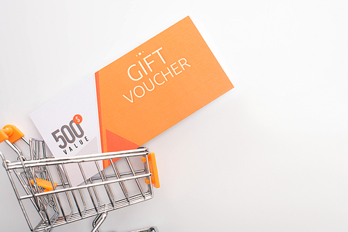 Top view of gift voucher with value lettering in toy shopping cart on white background