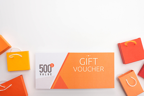 Top view of gift voucher with toy shopping bags on white background