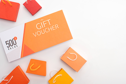 Top view of gift voucher near toy shopping bags on white surface
