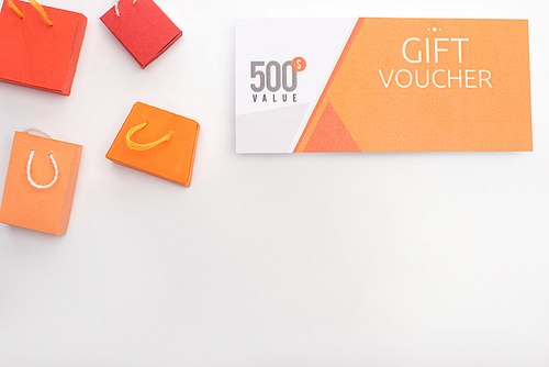 Top view of gift voucher with 500 dollars value lettering near toy shopping bags on white background with copy space