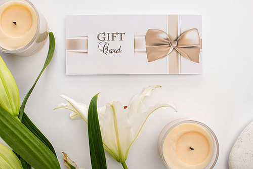 Top view of gift card, lily and candles on white background