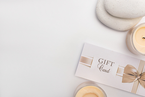 Top view of gift card, zen stones and candles on white background