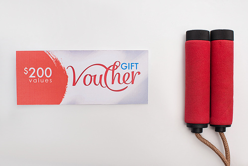 Top view of gift voucher with 200 dollars sign near jump rope on white background