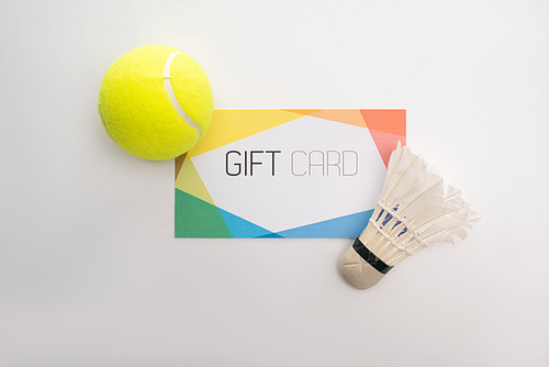 Top view of gift card near tennis ball and shuttlecock on white surface