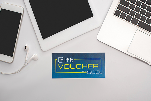 Top view of gift voucher near gadgets on white background