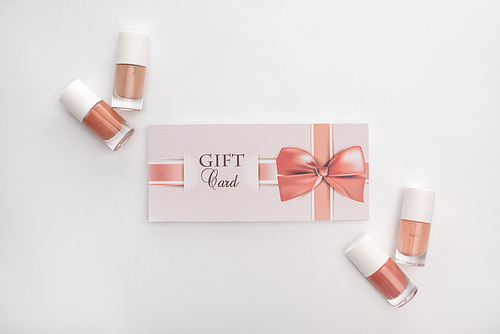 Top view of nail polishes and gift card with bow on white background