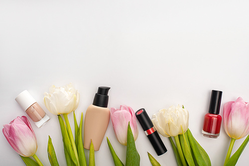 Top view of tulips with leaves and decorative cosmetics on white background