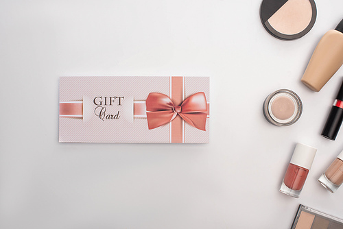 Top view of gift card near decorative cosmetics on white surface