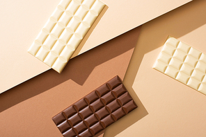 top view of delicious whole white and milk chocolate bars on beige background