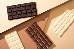 top view of delicious whole milk, white and dark chocolate bars on beige background