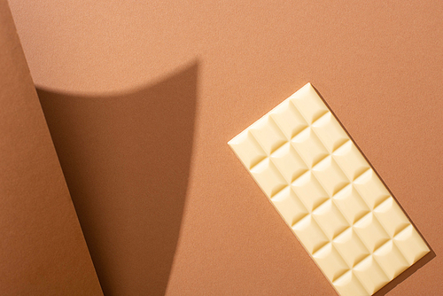 selective focus of delicious whole white chocolate bar on brown background with paper