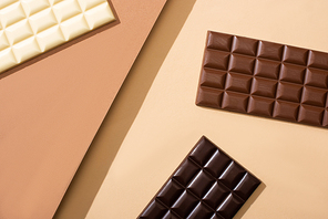 top view of delicious white, milk and dark chocolate bars on beige background