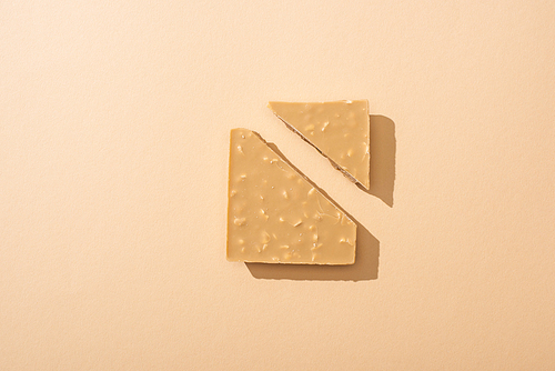 top view of delicious broken white chocolate bar on beige background