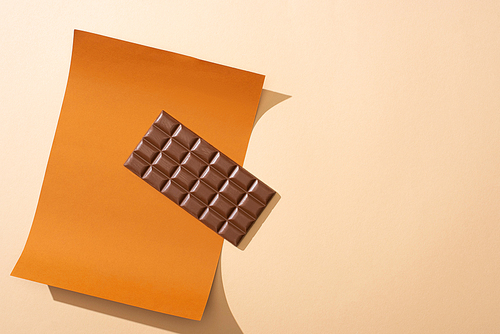 top view of delicious milk chocolate bar on paper on beige background