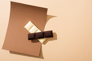 top view of delicious white and dark chocolate pieces on paper on beige background