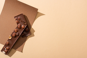 top view of delicious  milk chocolate with nuts pieces on paper on beige background