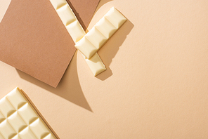 top view of delicious white chocolate pieces on paper on beige background