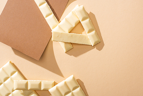 top view of delicious white chocolate pieces on paper on beige background