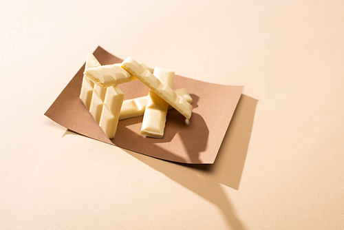 sweet delicious broken white chocolate bar on paper on beige background