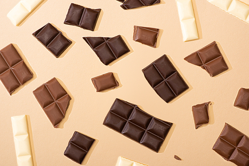 top view of delicious dark, milk and white chocolate pieces on beige background