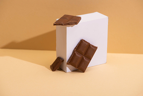 delicious milk chocolate pieces and square cube on beige background