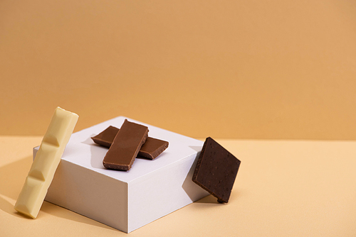 delicious white, dark and milk chocolate pieces and cube on beige background