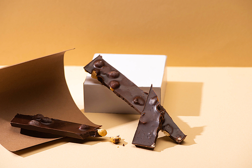 delicious dark chocolate with nuts pieces, paper and cube on beige background