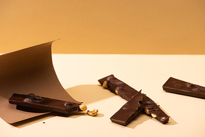 delicious dark chocolate with nuts pieces, paper on beige background