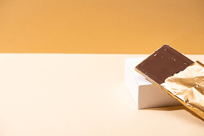 delicious milk chocolate bar in golden foil on cube on beige background