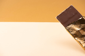 delicious milk chocolate bar in golden foil on beige background