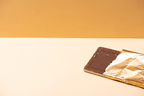 delicious milk chocolate bar in golden foil on beige background