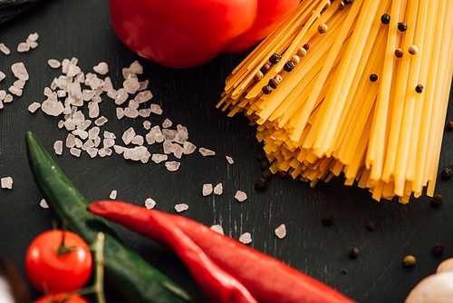 selective focus of raw Italian spaghetti with vegetables and salt on black background