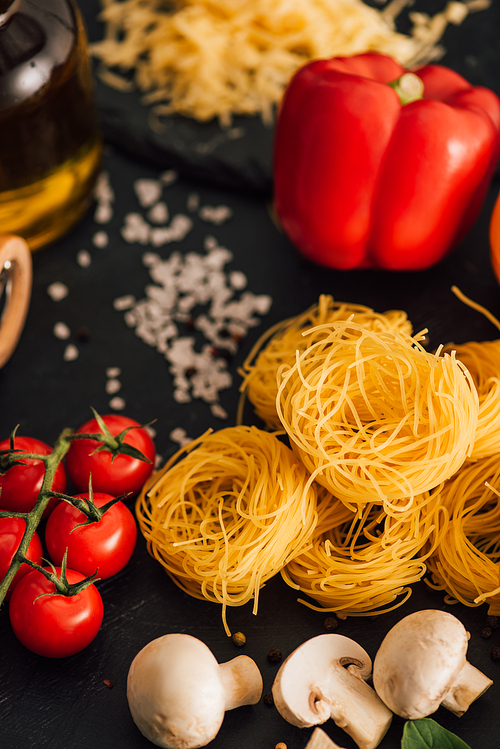 selective focus of raw Italian Capellini with vegetables and salt on black background