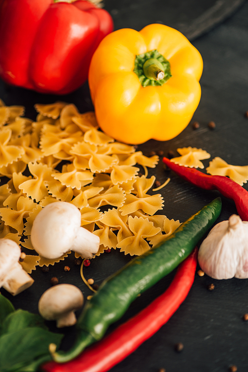 raw Italian farfalle with vegetables on black background