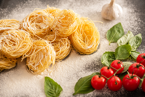 raw Italian Capellini with vegetables and flour on black background
