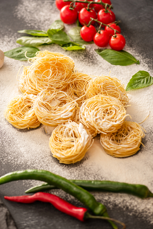raw Italian Capellini with vegetables on flour on black background