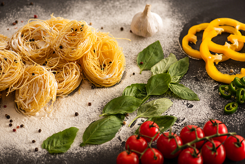raw Italian Capellini with vegetables on flour on black background