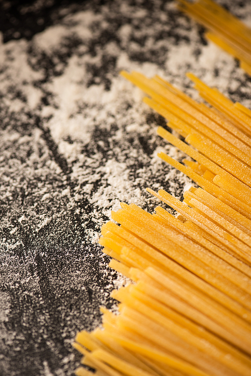 close up view of raw spaghetti and flour on black background