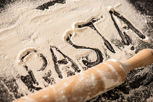 pasta lettering written on flour near rolling pin on black background