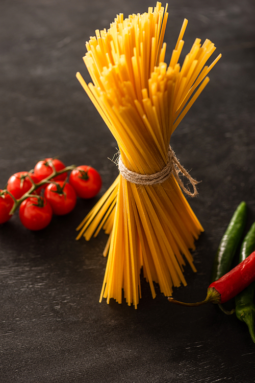 uncooked Italian spaghetti with tomatoes and chili peppers on black background