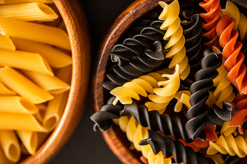 close up view of colorful raw Italian pasta in wooden bowls