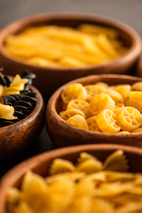 selective focus of raw fusilli and rotelle pasta in wooden bowls