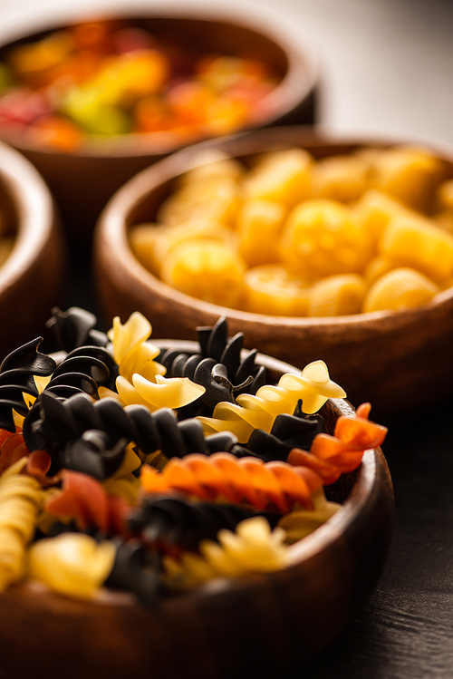 selective focus of colorful raw fusilli pasta in wooden bowl