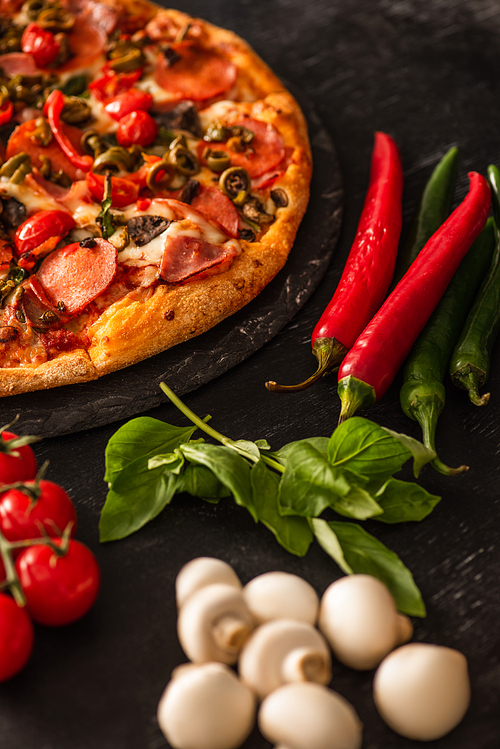 selective focus of delicious Italian pizza with salami near vegetables on black background